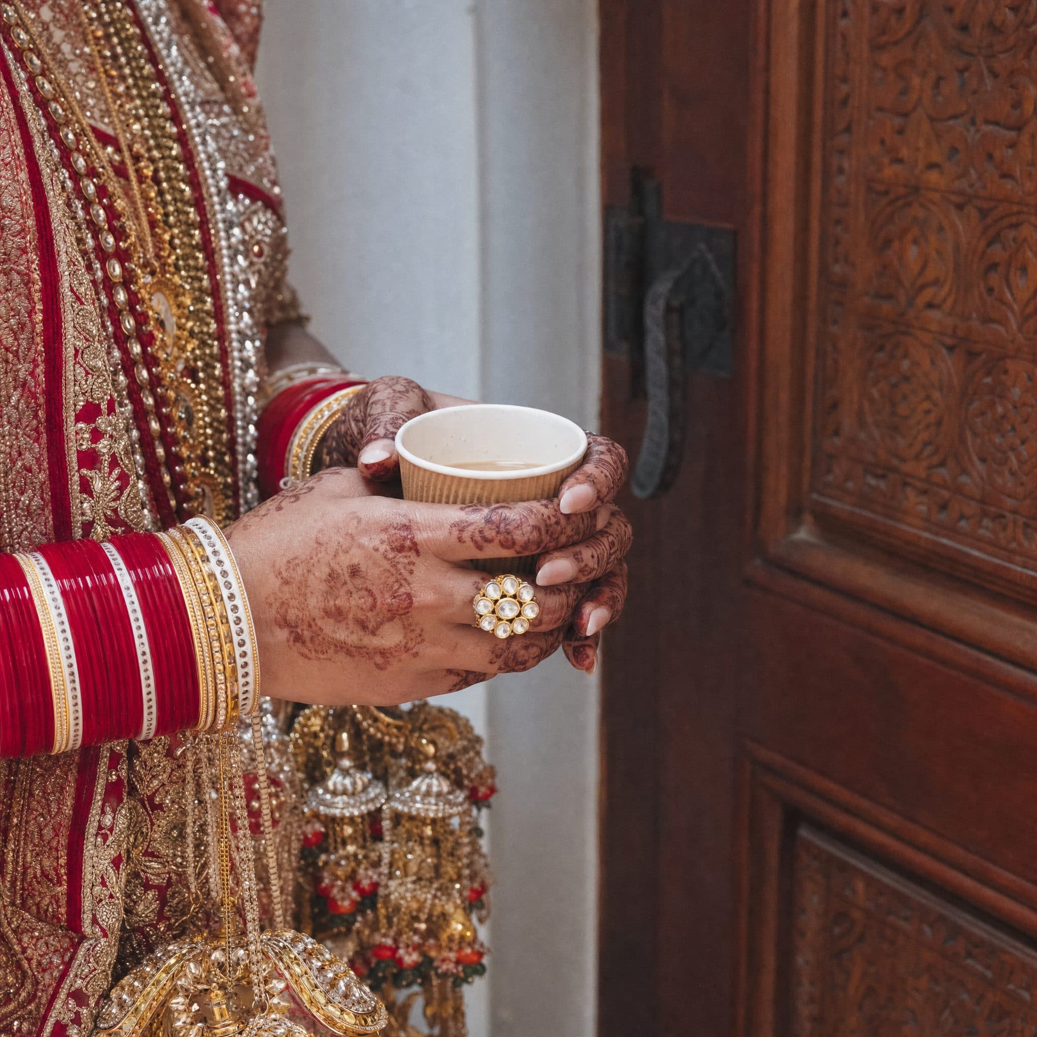 Henna-covered hands holding a cup of chai against a carved wooden door