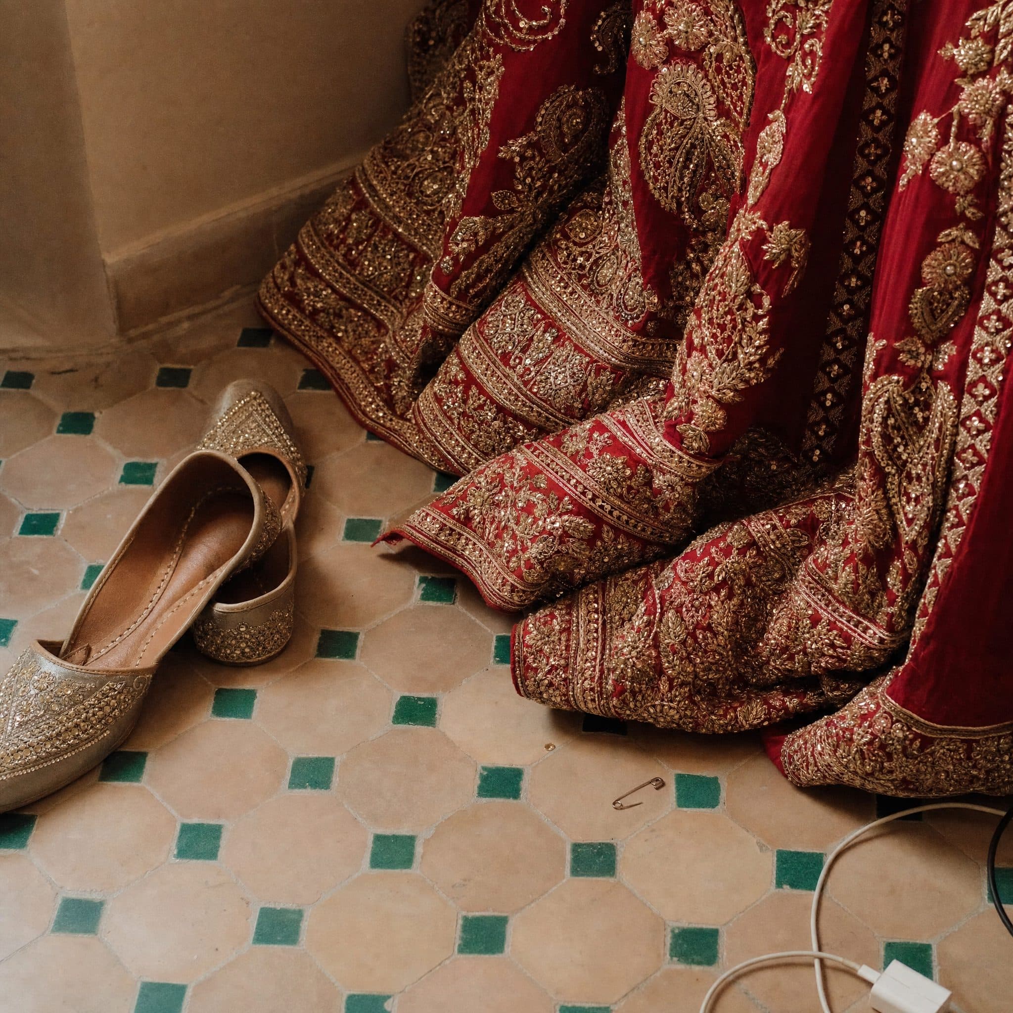 Bridal lehenga and gold juttis laid out on zellige tile