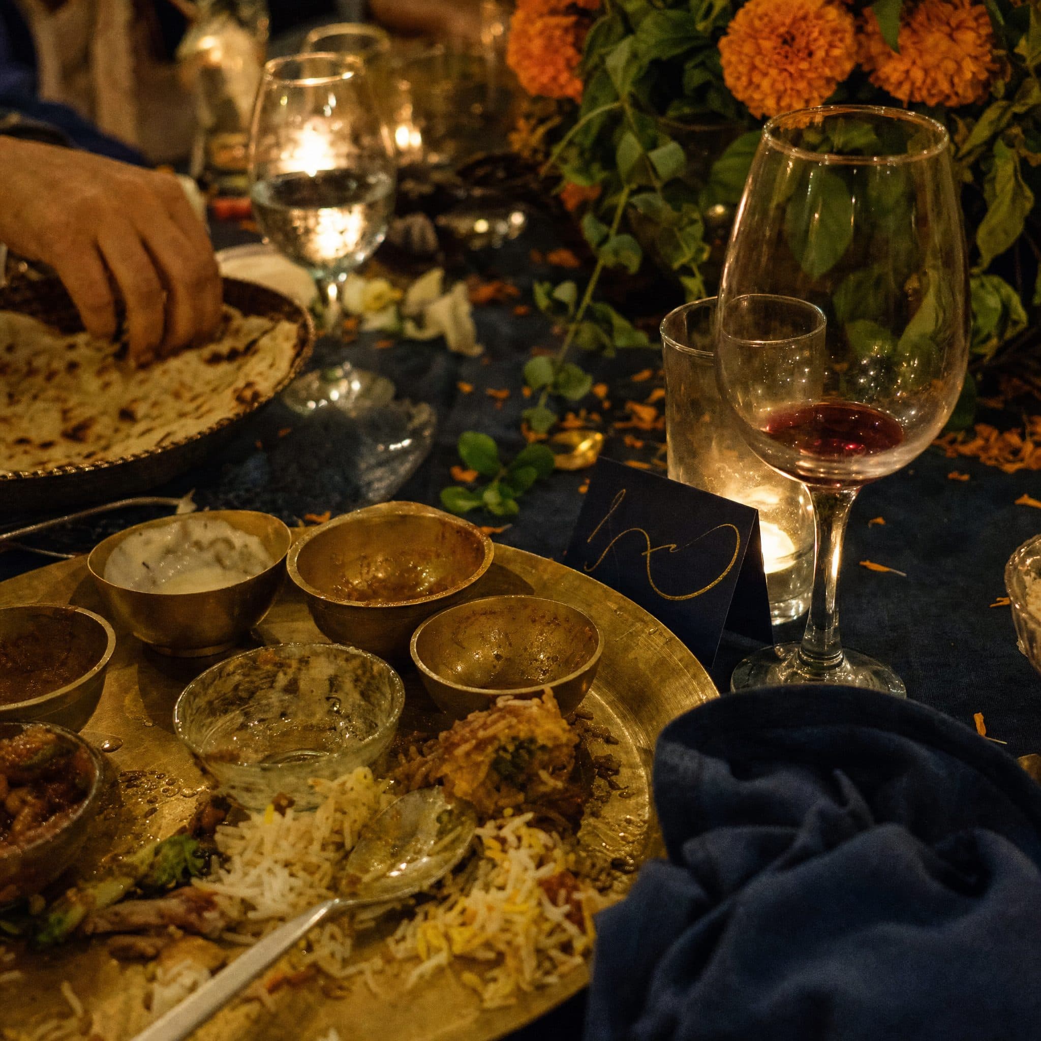 Brass thali of Indian dishes laid on a dark table with marigolds and candlelight