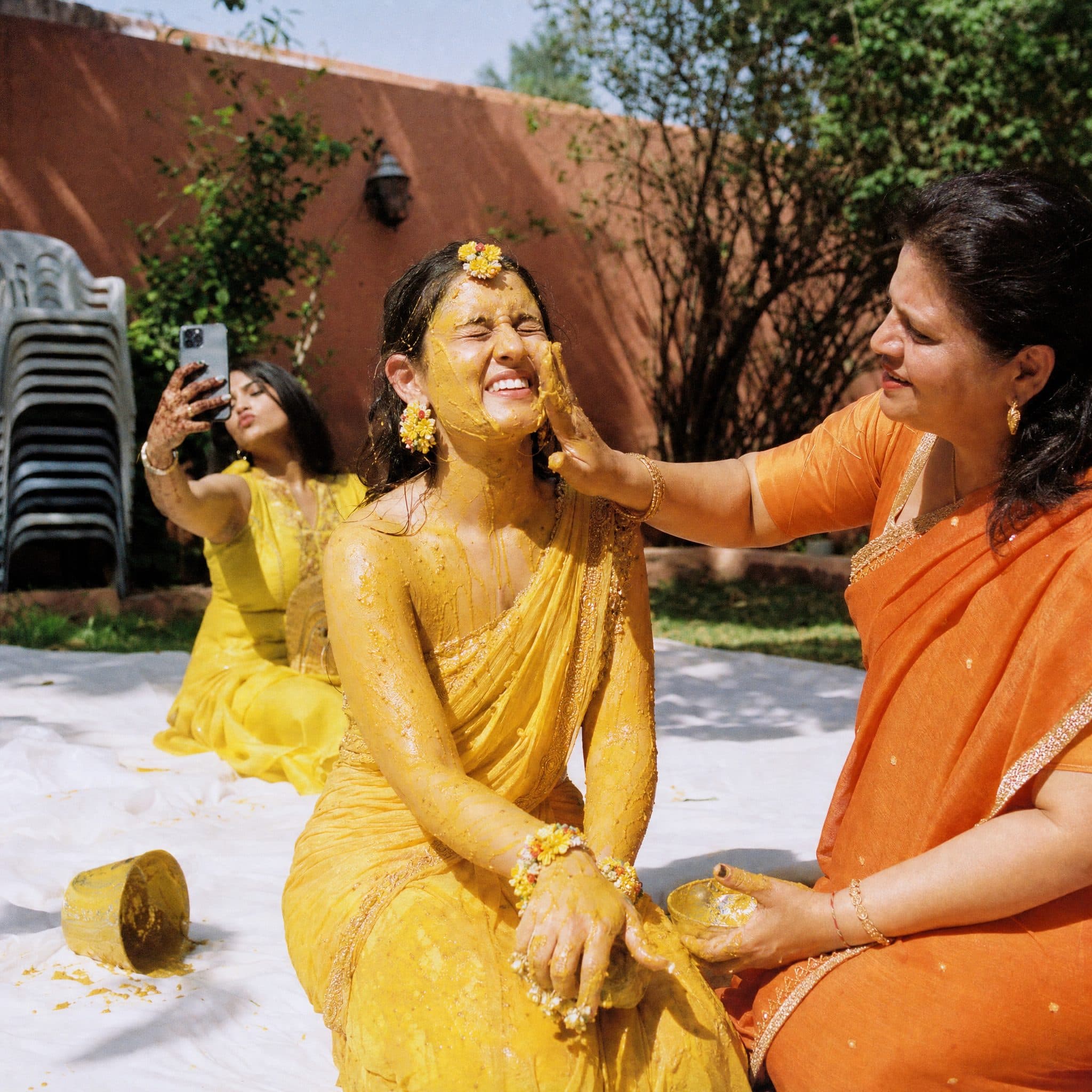 Bride laughing as turmeric is pressed to her cheek during Haldi