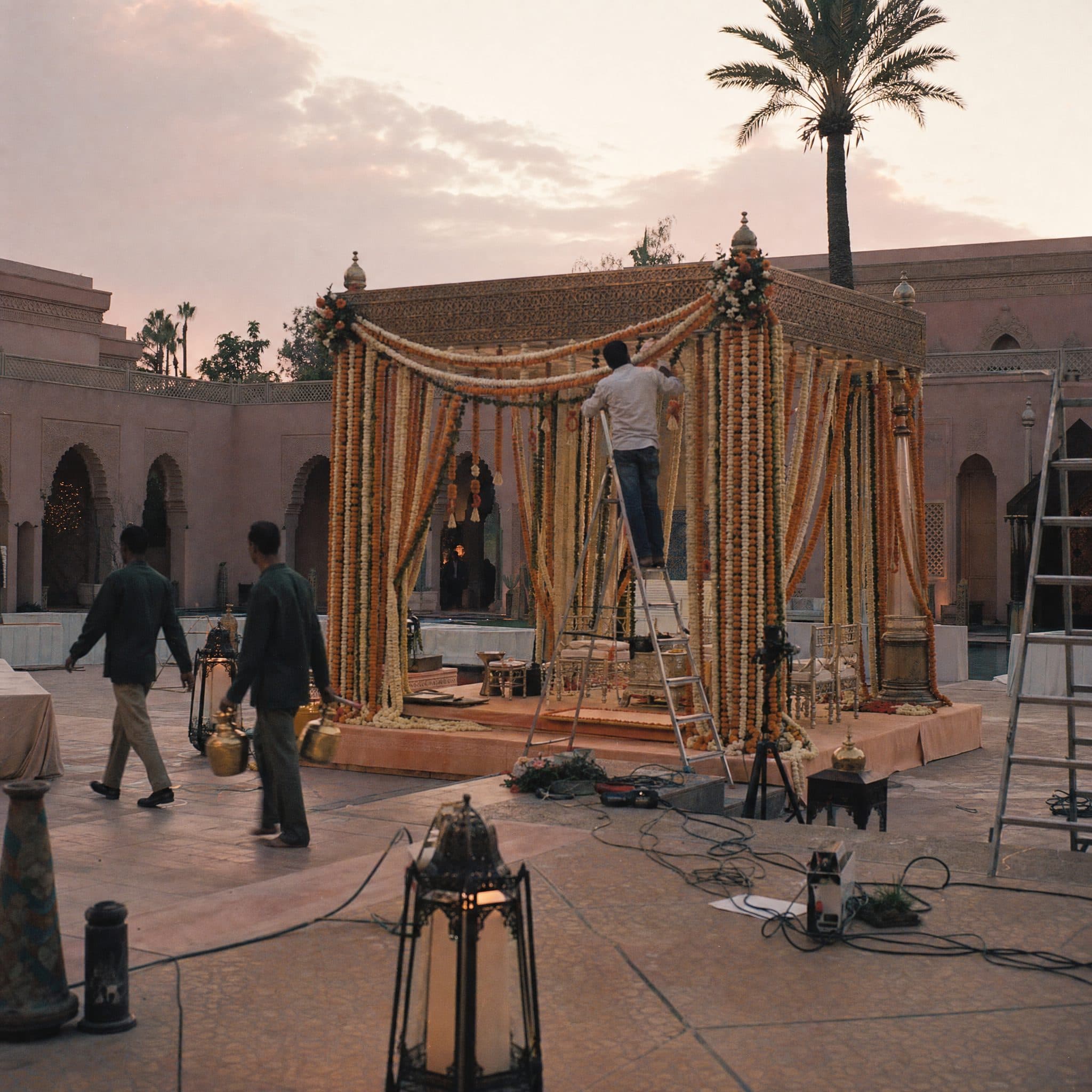 Crew building a marigold-draped mandap in a palace courtyard at dawn