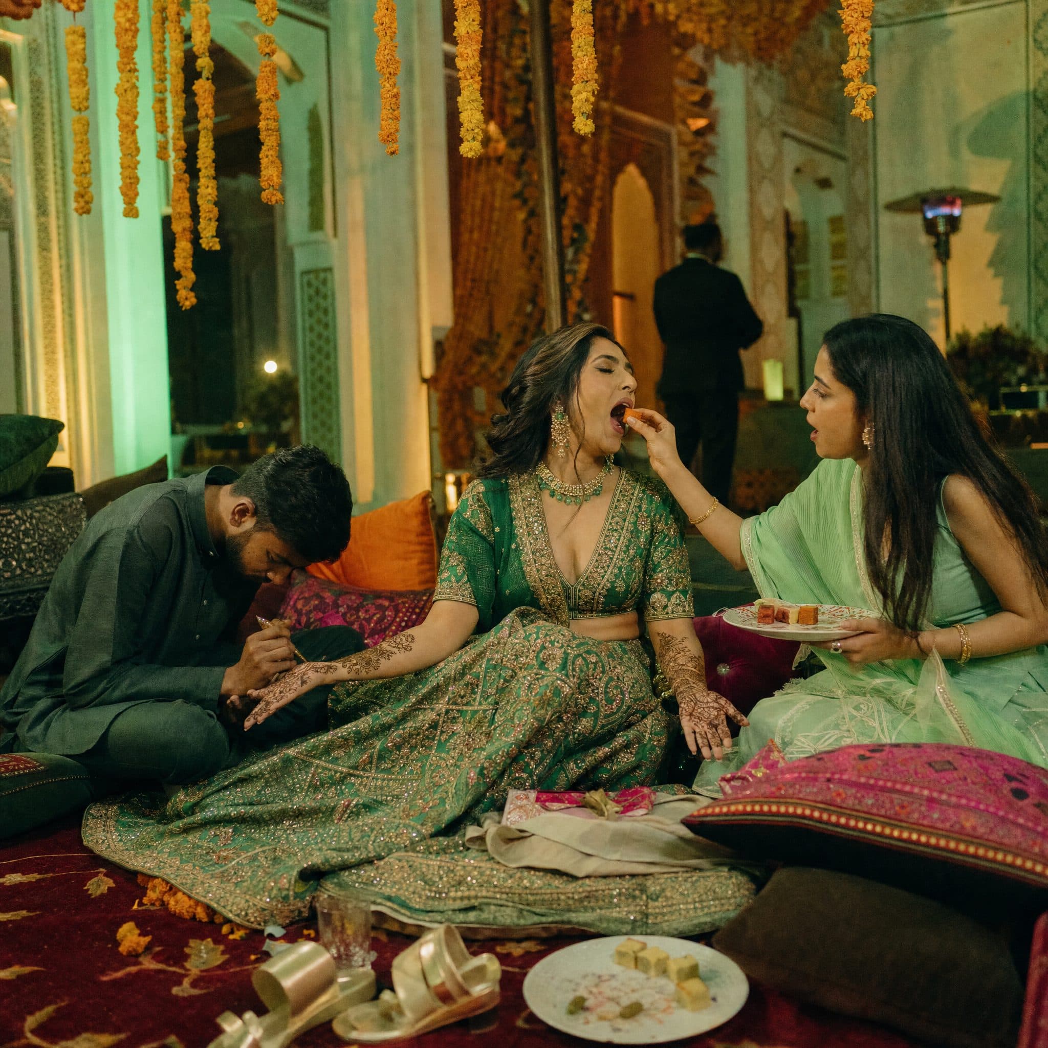 Bride in a green lehenga resting after her Mehndi while friends feed her sweets